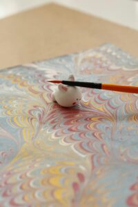 A miniature bunny on marbled paper with a paintbrush creating a delicate artistic effect.